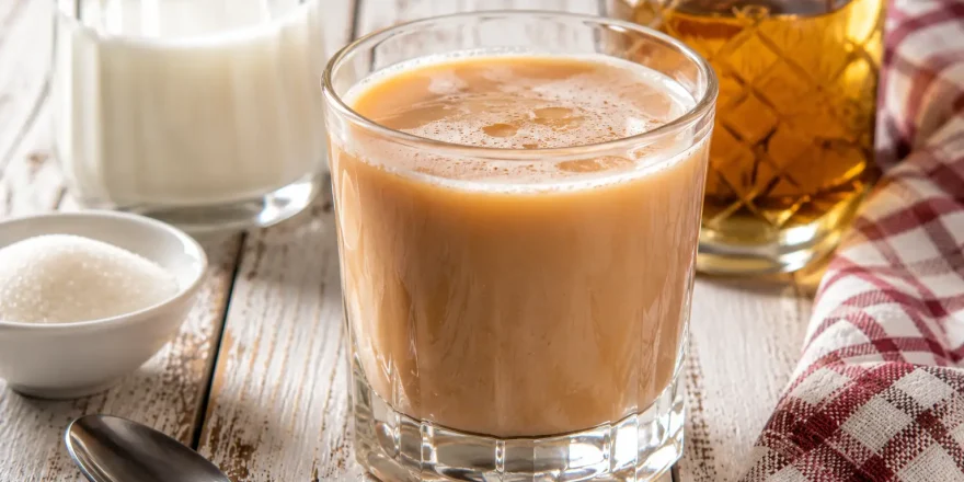 Tee-Mix mit Milch und Rum in Glas auf weißem Holztisch angerichtet