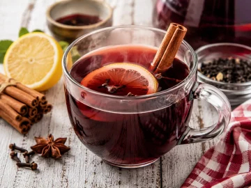 Ungarischer Punsch mit Zimt, Nelken und Zitrone in Tasse auf weißem Holztisch