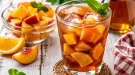 Vietnamesischer Fruchttee mit Eiswürfeln und Fruchtstücken in Glas auf weißem Holztisch