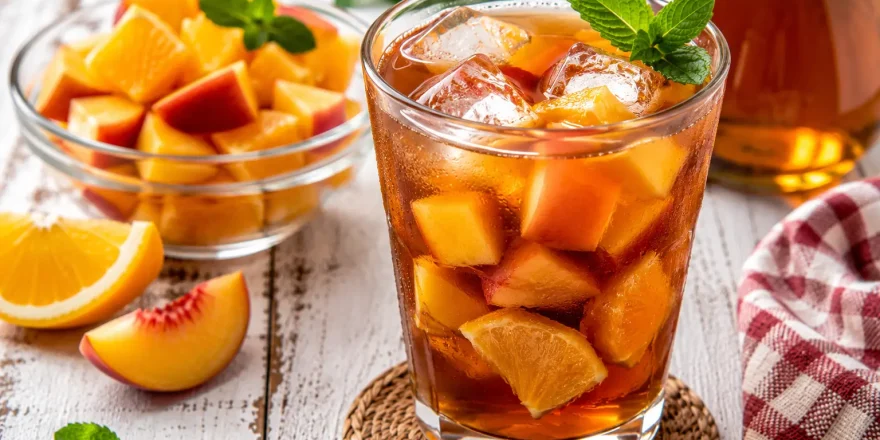 Vietnamesischer Fruchttee mit Eiswürfeln und Fruchtstücken in Glas auf weißem Holztisch