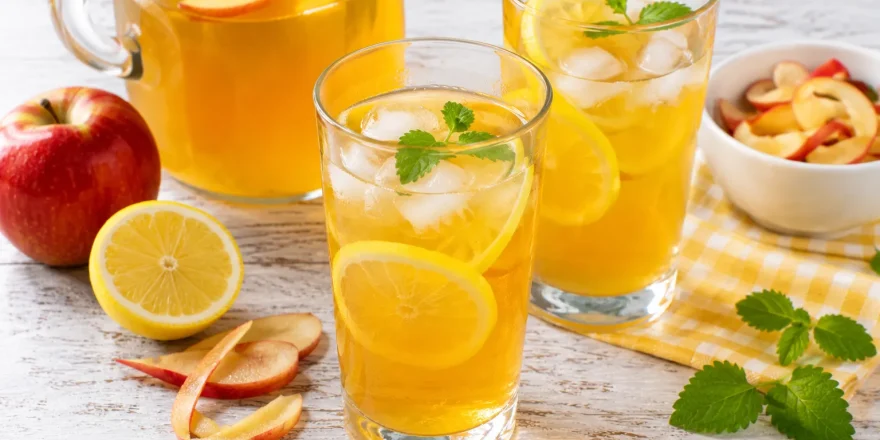 Erfrischende Apfeltee-Limonade mit Zitrone in modernen Gläsern auf rustikalem weißen Holztisch