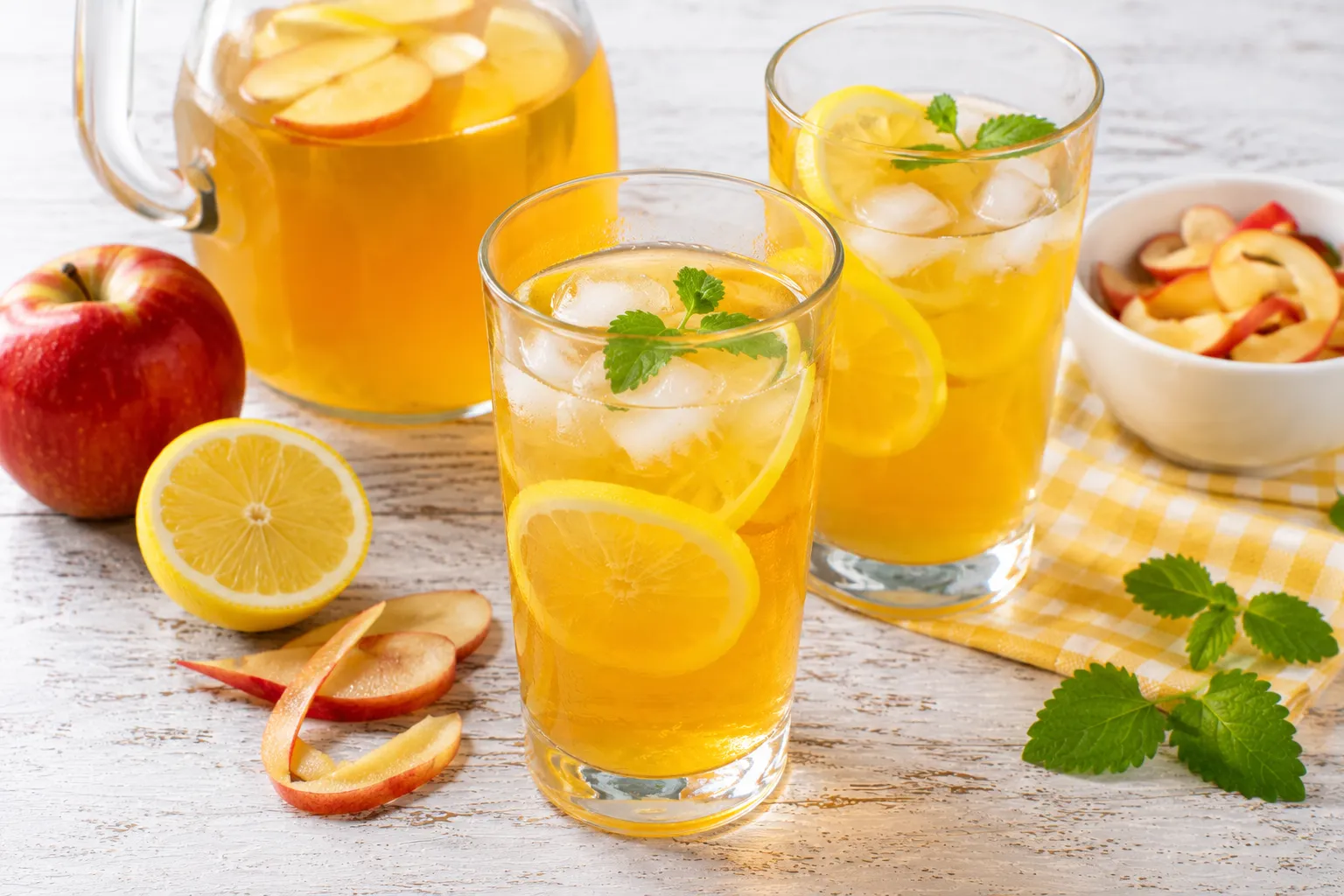 Erfrischende Apfeltee-Limonade mit Zitrone in modernen Gläsern auf rustikalem weißen Holztisch