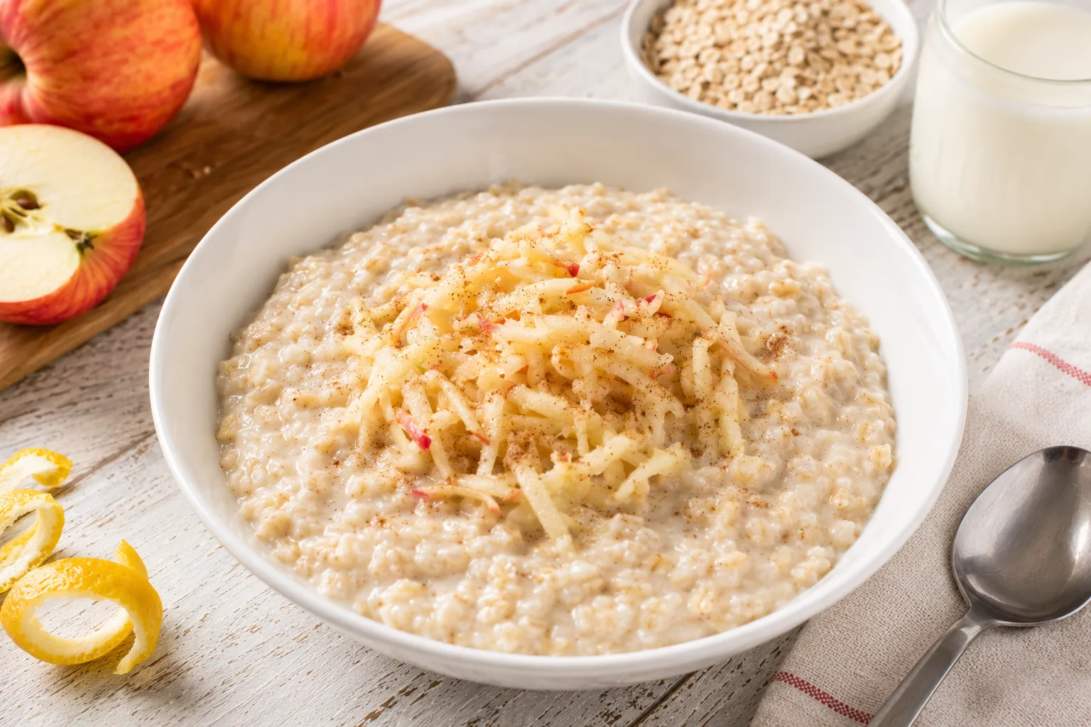 Cremiger Haferflockenbrei mit geriebenem Apfel in moderner weißer Schüssel auf rustikalem weißen Holztisch
