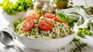 Weiße Schüssel mit cremigem Reissalat, grünen Erbsen und Tomatenscheiben auf rustikalem weißem Holztisch