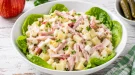 Frischer Schinkensalat mit Sellerie und Apfel in moderner weißer Schüssel auf rustikalem weißen Holztisch