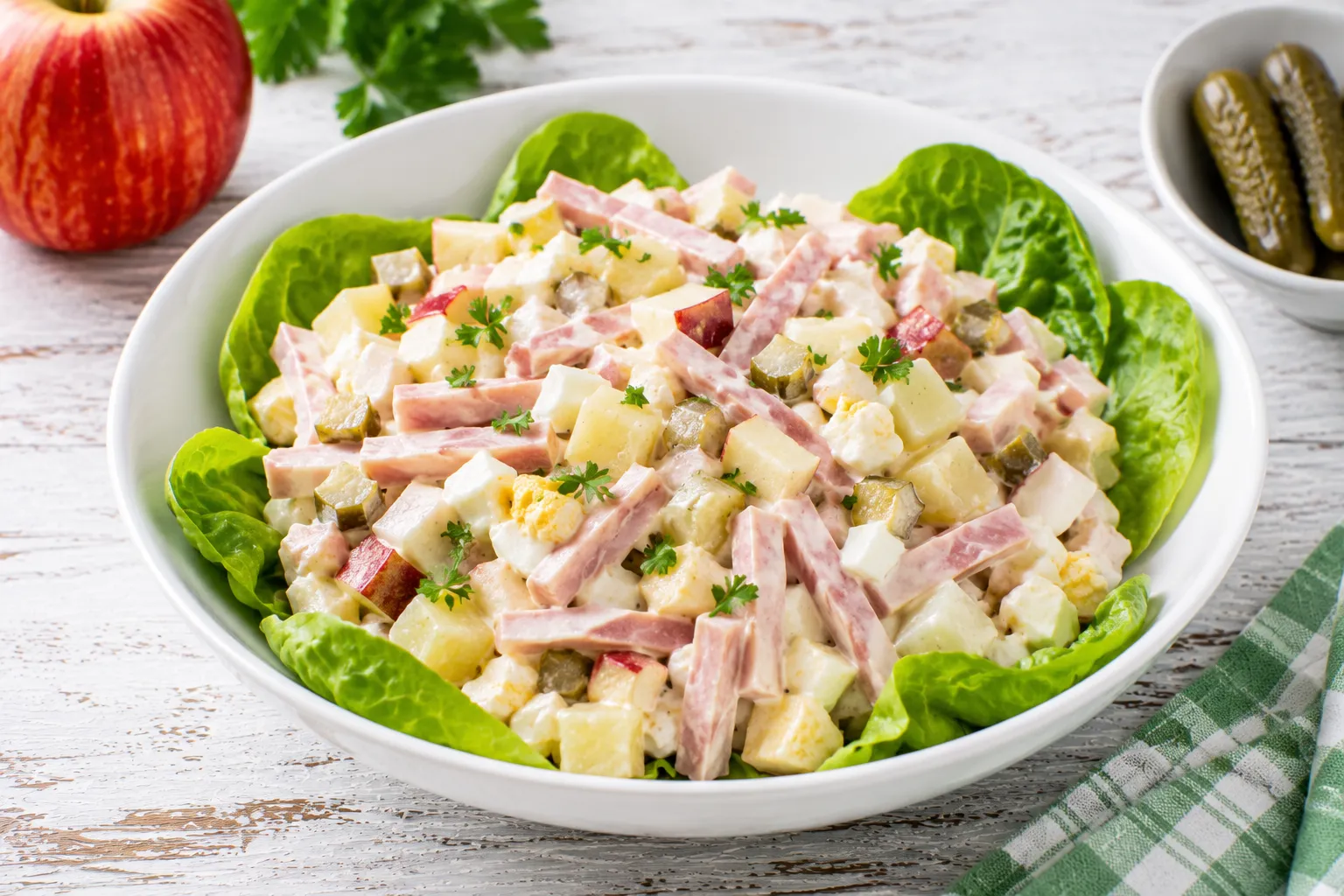 Frischer Schinkensalat mit Sellerie und Apfel in moderner weißer Schüssel auf rustikalem weißen Holztisch