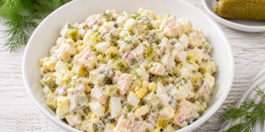 Schwedischer Fischsalat mit Ei und Gewürzgurke in moderner weißer Schüssel auf rustikalem weißen Holztisch
