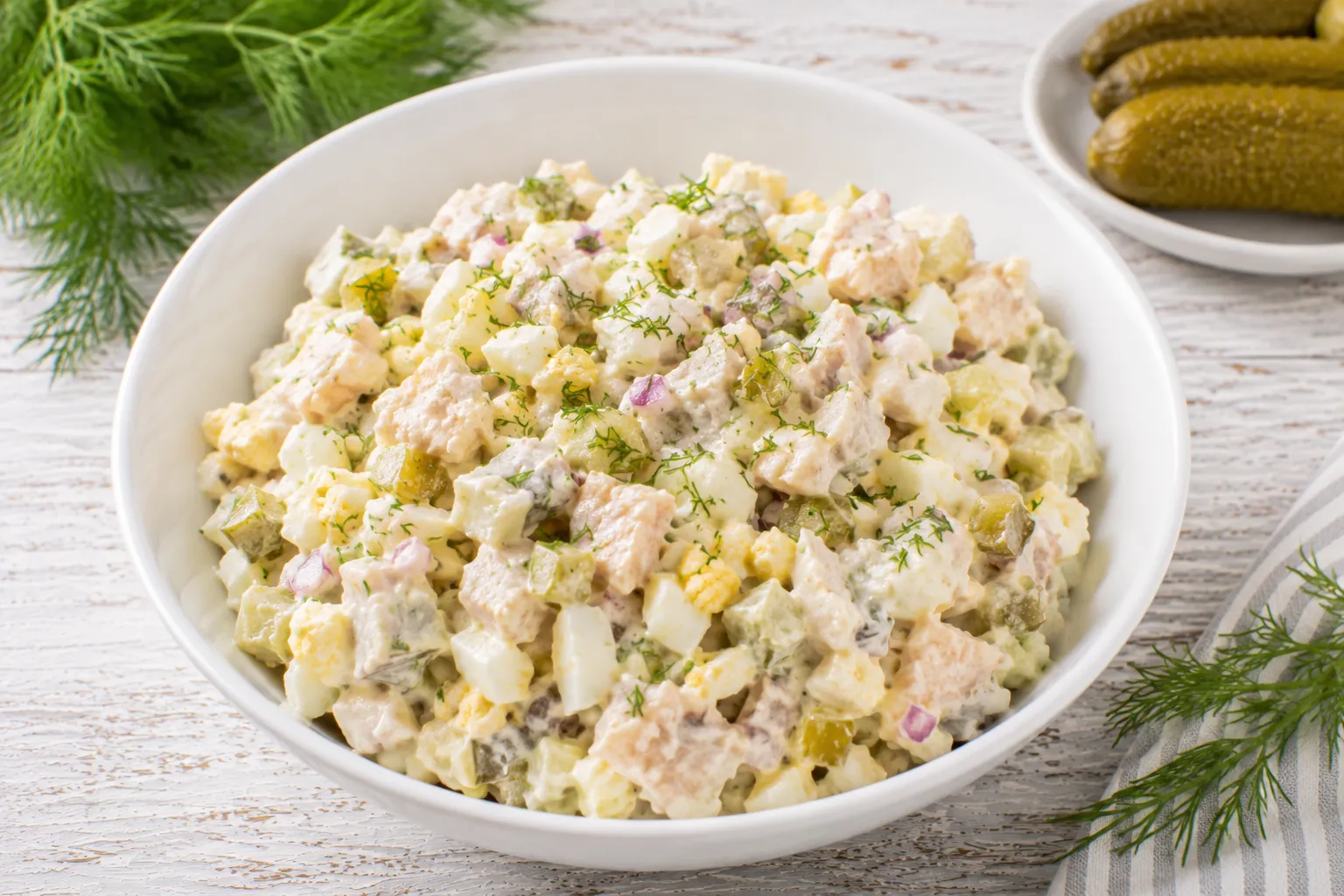 Schwedischer Fischsalat mit Ei und Gewürzgurke in moderner weißer Schüssel auf rustikalem weißen Holztisch