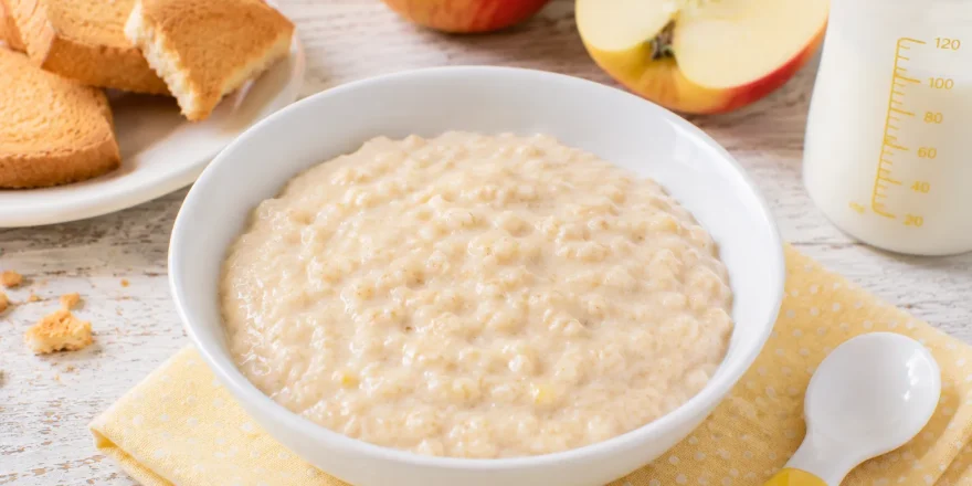 Cremiger Zwiebackbrei mit geriebenem Apfel in kleiner weißer Schüssel auf rustikalem weißen Holztisch