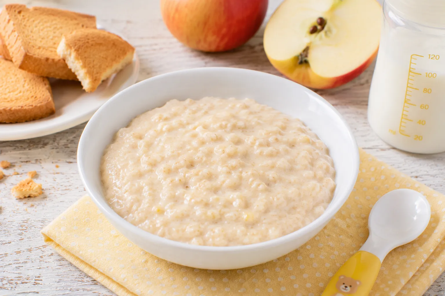 Cremiger Zwiebackbrei mit geriebenem Apfel in kleiner weißer Schüssel auf rustikalem weißen Holztisch