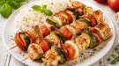 Geflügelspieße mit Gemüse und Speck auf weißem Teller serviert