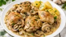 Geschmorte Hähnchenteile mit Champignons in cremiger Sahnesoße auf weißem Teller
