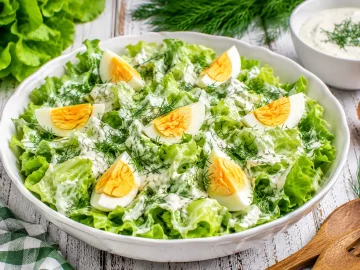 Knackiger Kopfsalat mit Sahnedressing, Dill und Eivierteln in weißer Salatschüssel