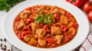 Putengulasch mit Paprika und Tomaten auf weißem Teller serviert