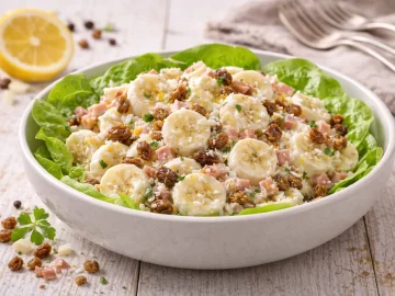 Afrikanischer Bananensalat mit Kokosraspeln und Sultaninen in moderner Salatschüssel auf hellem Holztisch