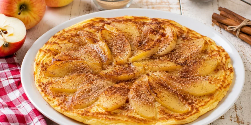 Apfel-Eierkuchen mit Apfelscheiben und Zimtzucker auf weißem Teller