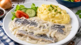 Bücklingsfilet in cremiger saurer Sahne mit Zwiebeln auf weißem Teller