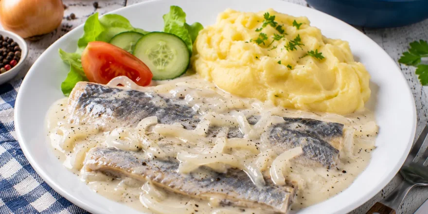Bücklingsfilet in cremiger saurer Sahne mit Zwiebeln auf weißem Teller