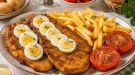 Knuspriges Rigaer Schnitzel mit hartgekochten Eiern, Pommes frites und gebratenen Tomaten.