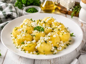 Kartoffeln mit zerbröseltem Schafskäse, Butter und frischen Kräutern auf einem modernen weißen Teller.