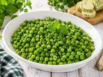 Frische grüne Erbsen in aromatischer Minzbutter mit Petersilie in einer modernen weißen Servierschüssel.