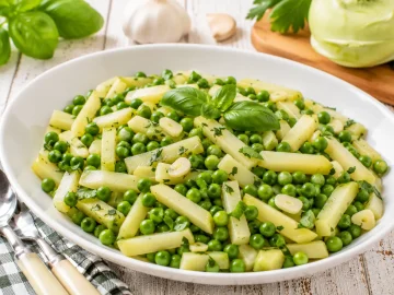 Erbsen-Kohlrabi-Gemüse mit frischem Basilikum und Knoblauch in einer modernen weißen Servierschüssel.