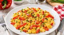 Lockeres Paprika-Rührei mit roten Paprikastreifen und frischem Schnittlauch auf einem modernen weißen Teller.