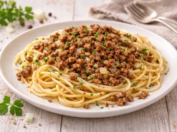 Spaghetti mit gebratenen Hackfleischbröseln und Zwiebeln auf hellem Teller auf weißem Holztisch