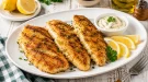 Knusprig gegrillte Fischfilets mit Zitrone und Remoulade auf einem modernen weißen Teller.