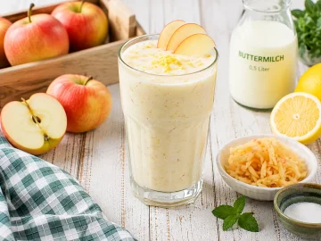 Cremige Apfel-Buttermilch in einem hohen Glas mit Apfelscheiben und Zitronenschale.