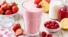 Cremiger Fruchtsaftmix mit Erdbeer- und Himbeersaft in einem hohen Glas mit frischen Beeren.