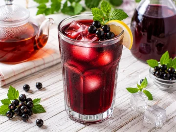 Kalter Johann in einem hohen Glas mit Eiswürfeln und frischen schwarzen Johannisbeeren.