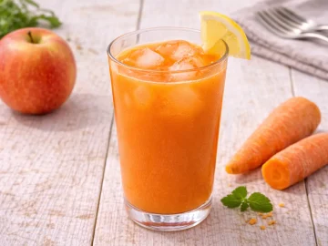 Möhren-Apfel-Drink mit Eiswürfeln in Glas auf hellem Holztisch