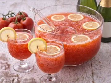 Tomaten-Bowle in Bowleschüssel mit Zitronenscheiben und zwei Gläsern auf weißem Holzhintergrund