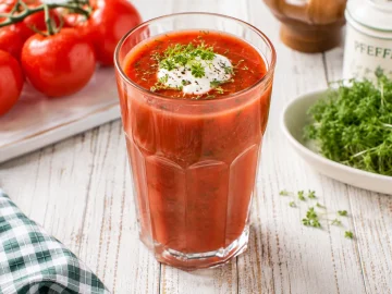 Herzhafter Vitamin-Drink aus Tomatensaft mit Kresse und einem Klecks saurer Sahne in einem hohen Glas.