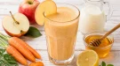 Cremiger Apfel-Möhren-Drink mit Honig in einem hohen Glas.