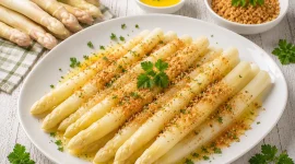 Gekochter weißer Spargel mit Butter und gerösteten Semmelbröseln auf einer Servierplatte.