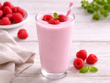 Himbeer-Buttermilch mit frischen Himbeeren in einem Glas auf hellem Holztisch
