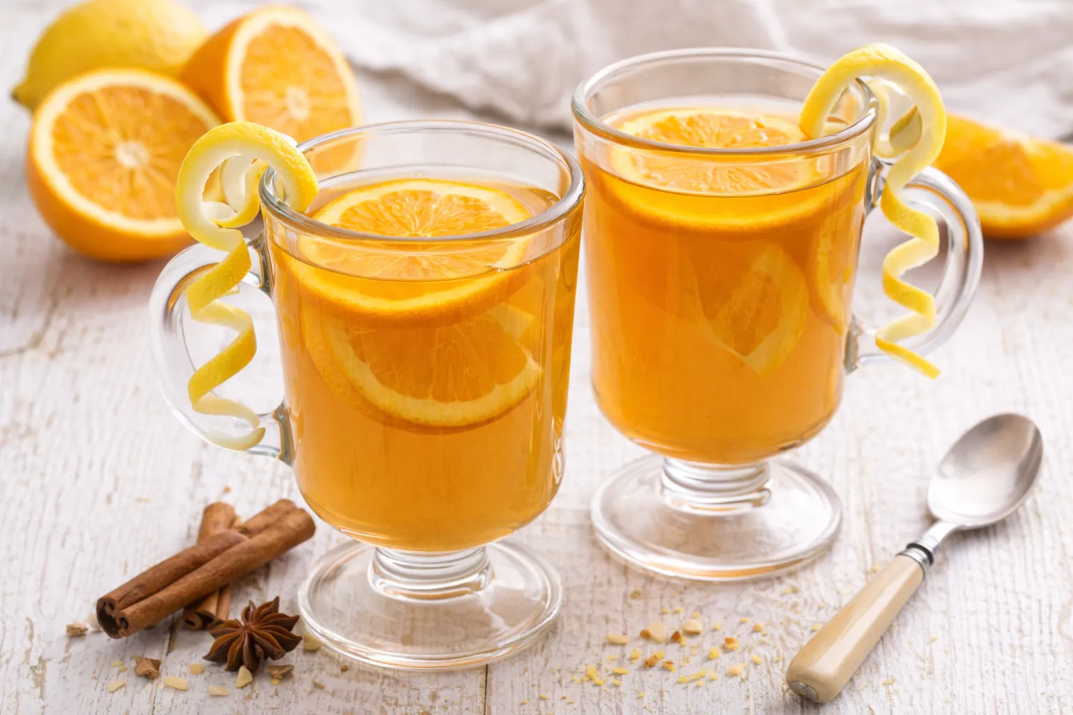 Heißer Kinderpunsch in Glasbechern mit Orangenscheiben und Zitronenspirale auf weißem Holzhintergrund