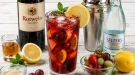Rotwein-Cooler mit Eiswürfeln, Früchten und Zitronenscheibe in einem hohen Glas.