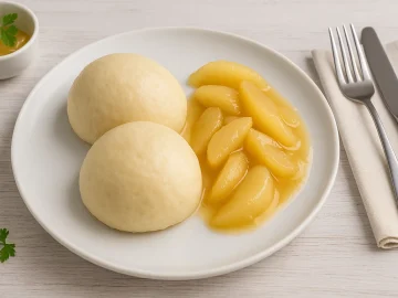 Zwei fluffige Hefeklöße mit süßem Birnenkompott, serviert auf weißem Teller mit Besteck auf hellem Holztisch