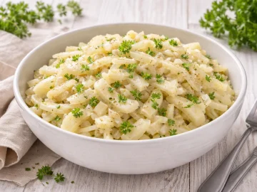 Schüssel mit mariniertem Selleriesalat auf weißem Holztisch mit Besteck