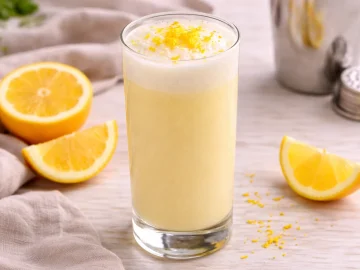 Zitronenflip mit Eigelb, Sahne und Weißwein in hohem Glas, garniert mit Zitronenschale auf hellem Holztisch.