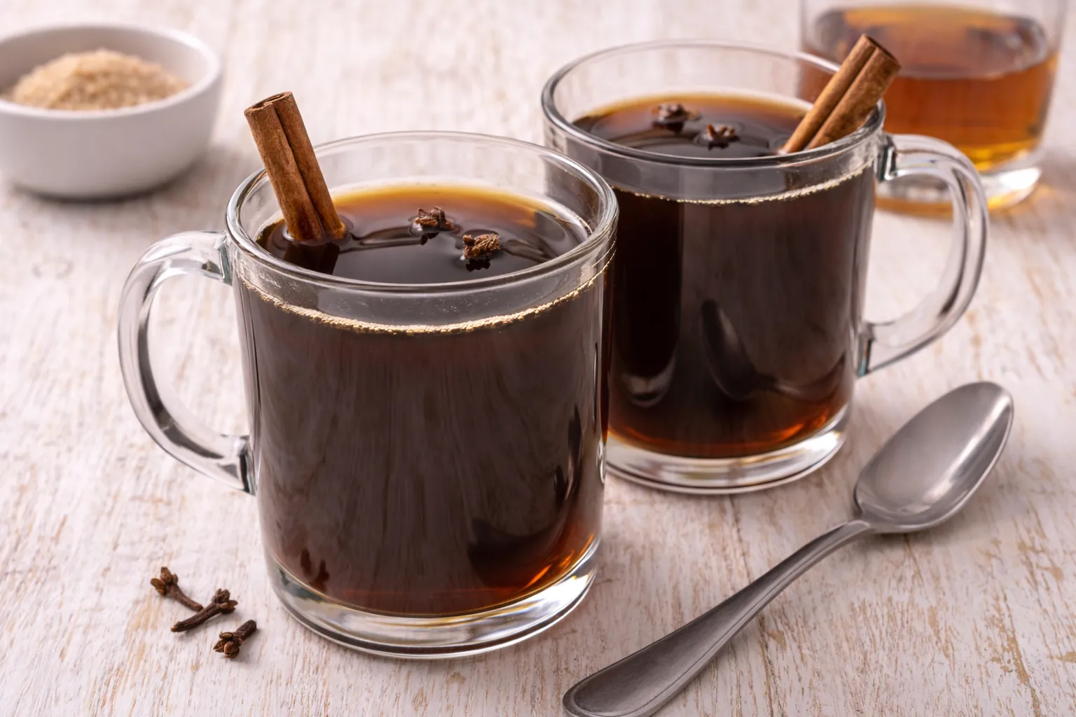 Heißer Kaffee mit Zimtstange und Nelken im Glas auf hellem Holztisch