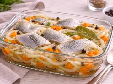 Marinierte Salzheringe mit Möhren, Zwiebeln und Gewürzen in Glasgefäß auf hellem Holztisch.