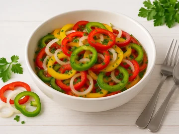 Weiße Schüssel mit buntem Paprikasalat, roten, gelben und grünen Paprikaringen, Zwiebeln und Petersilie auf weißem Holztisch