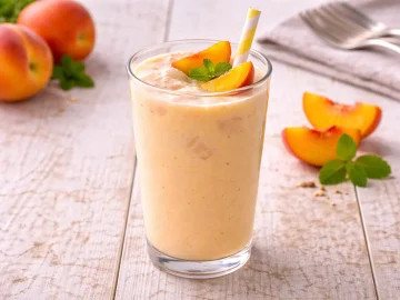 Pfirsich-Cocktail mit Milch und Pfirsichen in hohem Glas auf hellem Holztisch