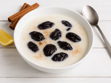 Altberliner Milchsuppe mit Pflaumen in weißem tiefen Teller, dekoriert mit Zimtstange und frischer Zitrone