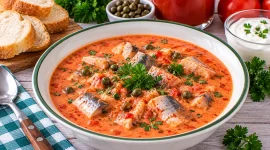 Cremige rote Fischsuppe mit Heringsstücken, Kapern und Petersilie.