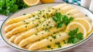 Weiße Spargelspitzen mit Kräuterbutter, Zitronenscheibe und Petersilie.